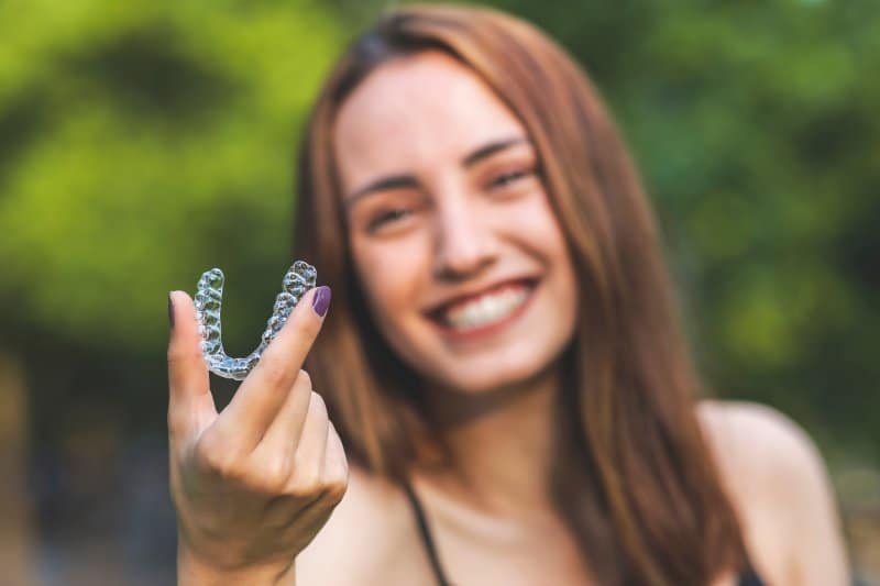 girl smiling and holding up Invisalign clear aligner